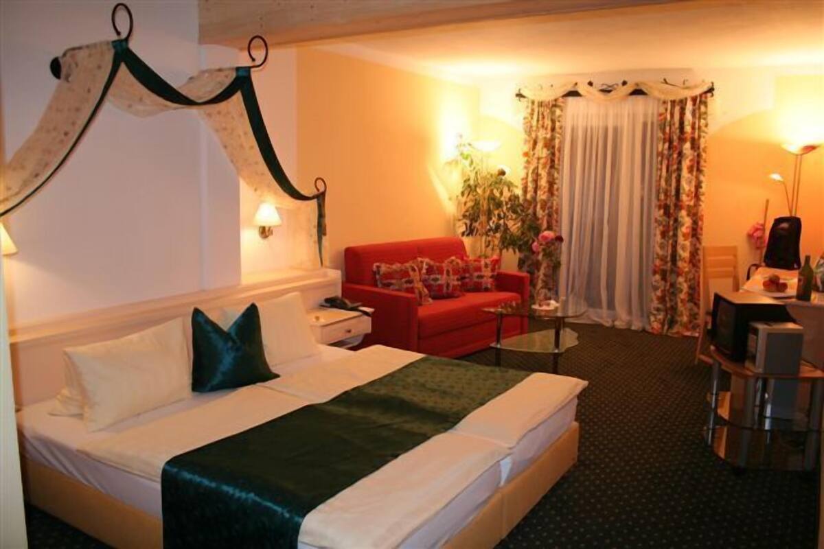 A hotel room with a bed, a red sofa, a small table, and a television.
