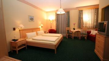 Una habitación de hotel con cama, mesitas de noche, un escritorio con silla, televisión y ventana con cortinas.