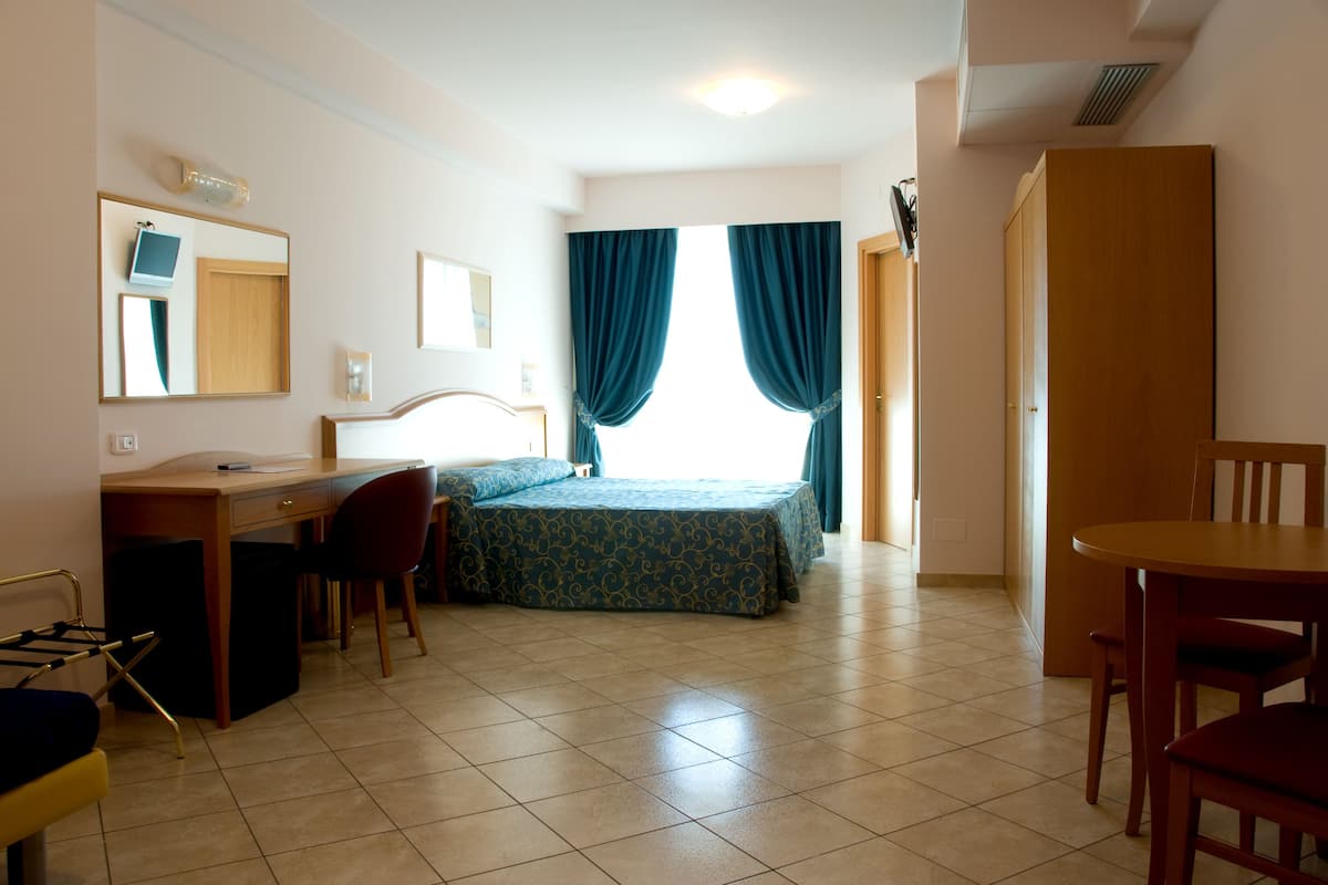 A room with a bed, a desk, a chair, a table, and a wardrobe.
