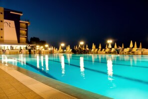 Une piscine entourée de chaises longues et de parasols, le tout bordé par un bâtiment sur lequel on peut voir un logo.