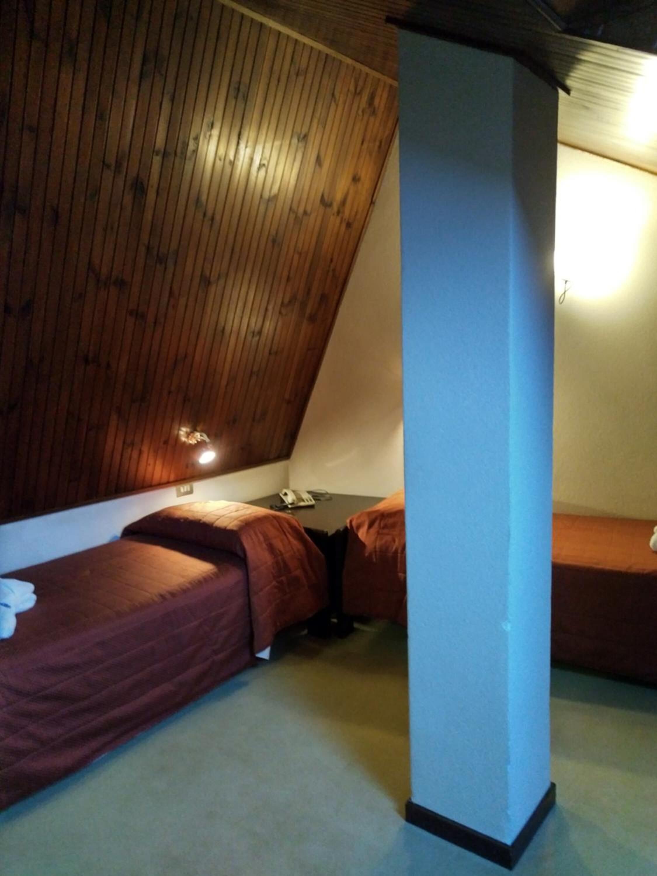 A small, dimly lit room with two single beds, a wooden sloped ceiling, and a single light source.