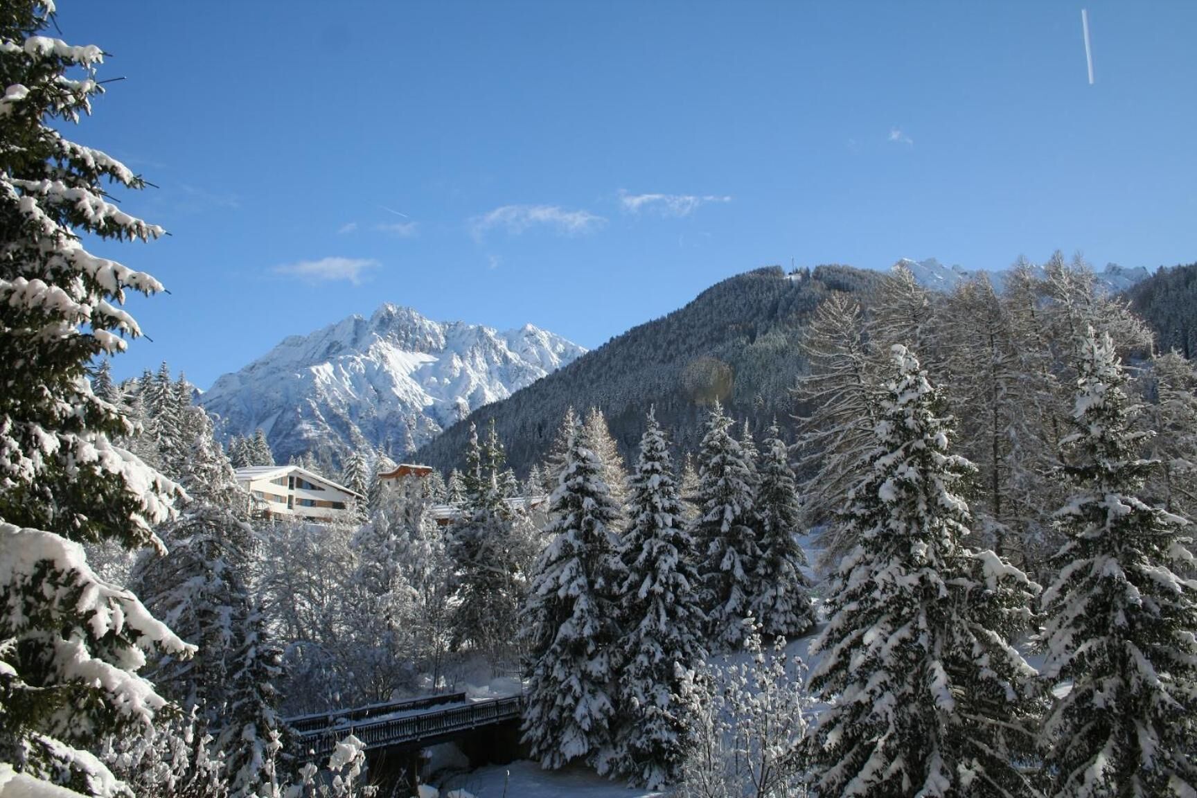 Un paysage enneigé avec une montagne en arrière-plan, un pont et un bâtiment doté d’un toit en pente.