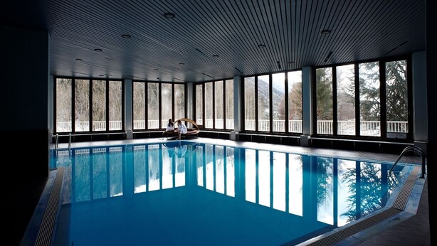 Una piscina interior con vistas a árboles a través de amplios ventanales.
