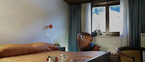 Habitación de hotel con una cama grande, techo de madera, ventana con cortinas, una silla y una mesa.