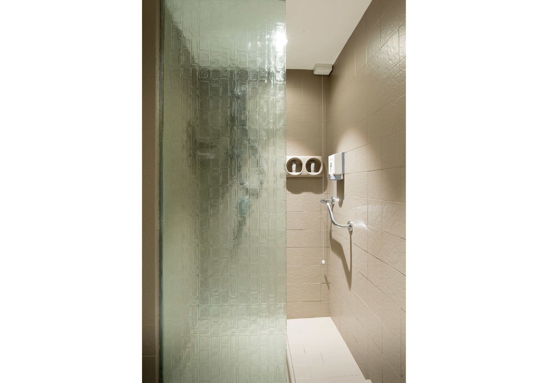 A bathroom with a glass shower door, a toilet paper holder, and a hand dryer on the wall.