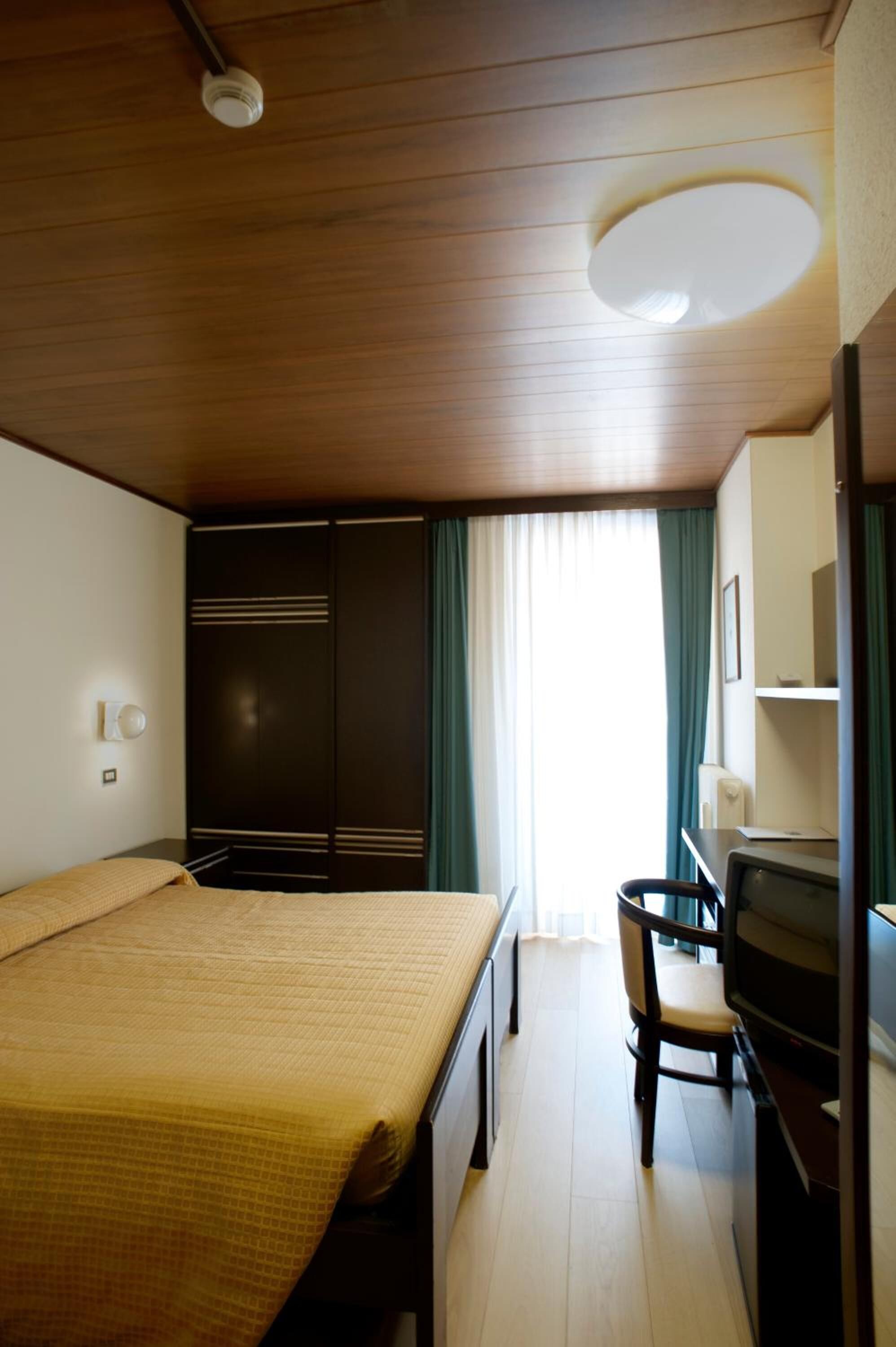 Ein Hotelzimmer mit einem Bett, einem Schreibtisch mit Stuhl, einem Fernseher und einem Kleiderschrank.