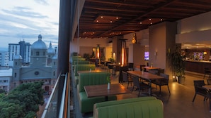 A restaurant with green booths, wooden tables, and a cityscape view in the background. - Hotel Soratama (Pereira)