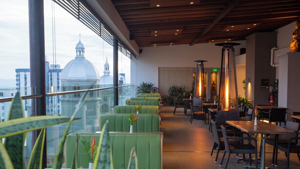 A rooftop restaurant with green seating, a view of a dome building, and a cityscape. - Hotel Soratama (Pereira)