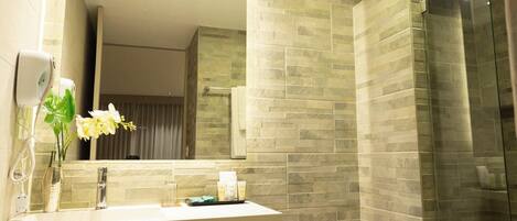 Un baño moderno con salpicadero de baldosas de piedra, tocador de madera, inodoro blanco y cabina de ducha de vidrio.