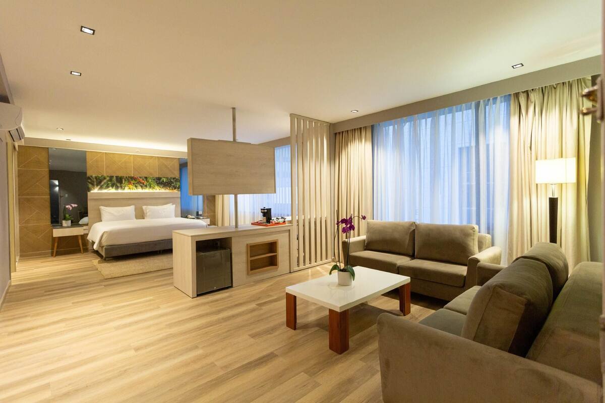 A modern hotel room with a bed, a sofa, a coffee table, and a desk.