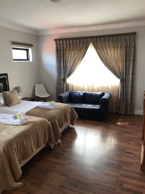 A hotel room with two beds, a sofa, a small table, and a window with curtains. - Albatross Guest House (Cape Town)