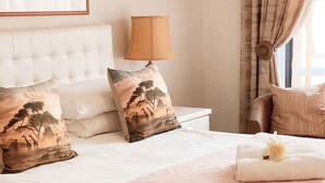 A neatly made bed with a quilted cover, two pillows with a nature scene design, a bedside lamp, and a framed artwork on the wall. - Albatross Guest House (Cape Town)