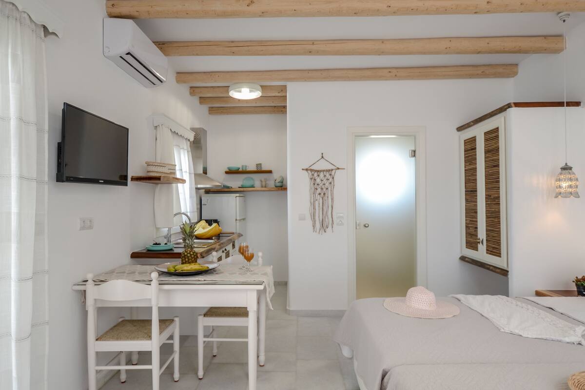 A room with a bed, a desk with a chair, a television, and a kitchenette.
