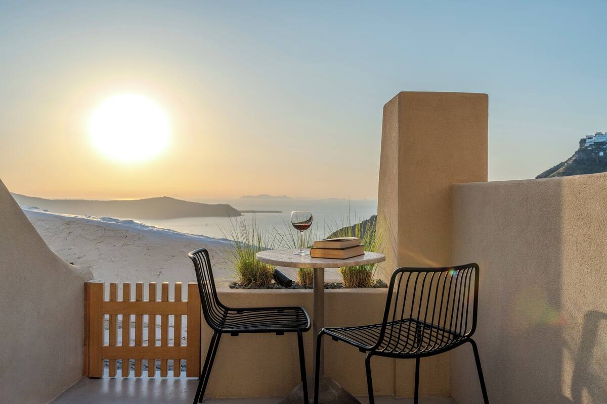 A balcony with a table, two chairs, a book, and a glass of wine.