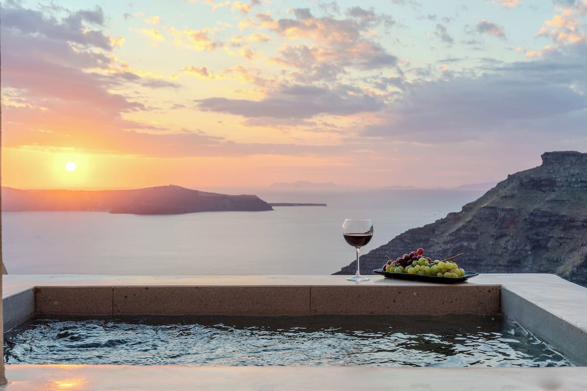 A sunset view from a balcony with a glass of wine and a plate of grapes.