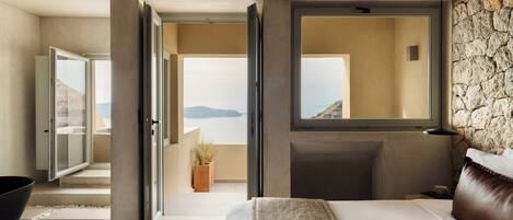 Une chambre moderne avec un grand lit, un mur en pierre et une vue sur la mer.