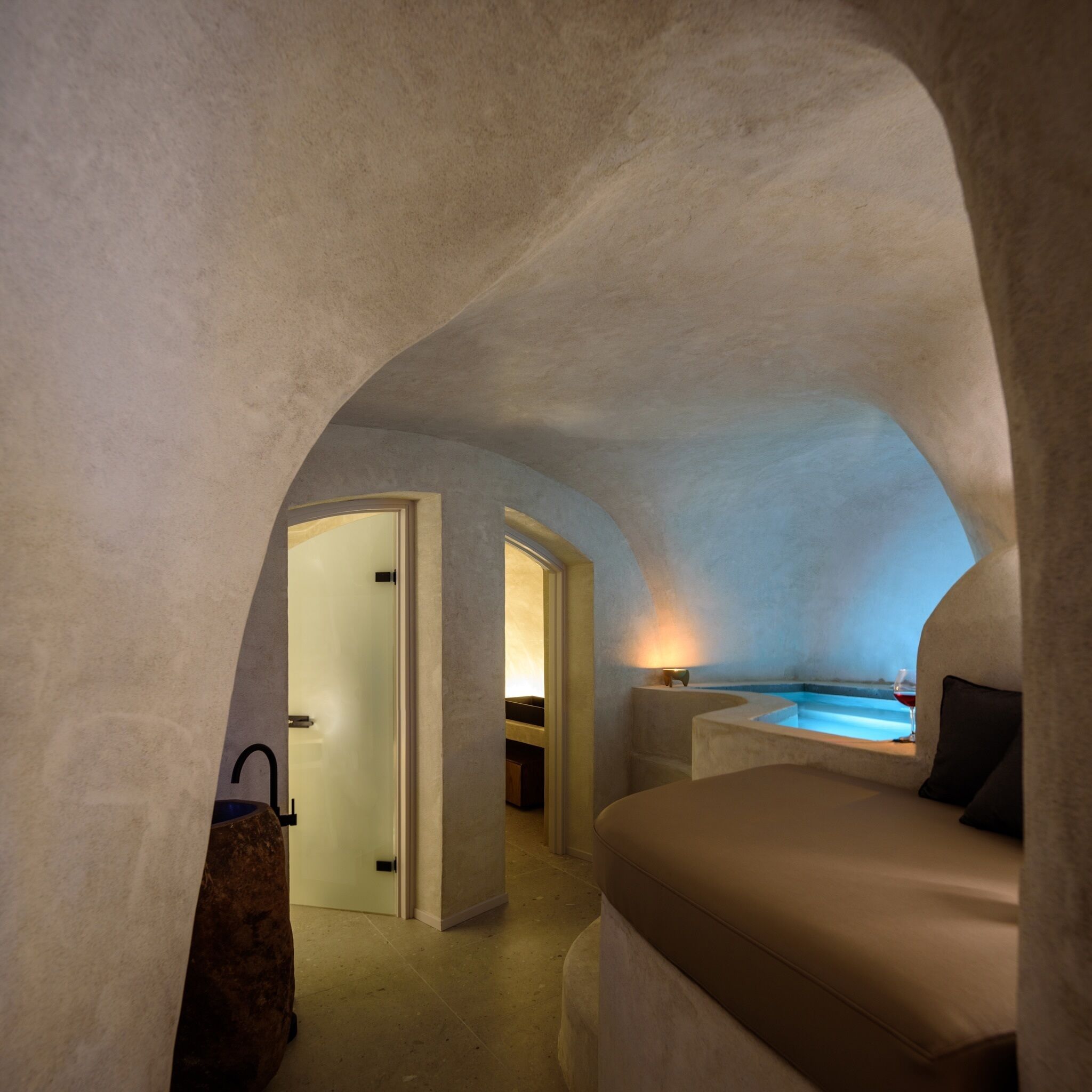 A cozy, arched room with a bed, a small table, and a view of a pool.