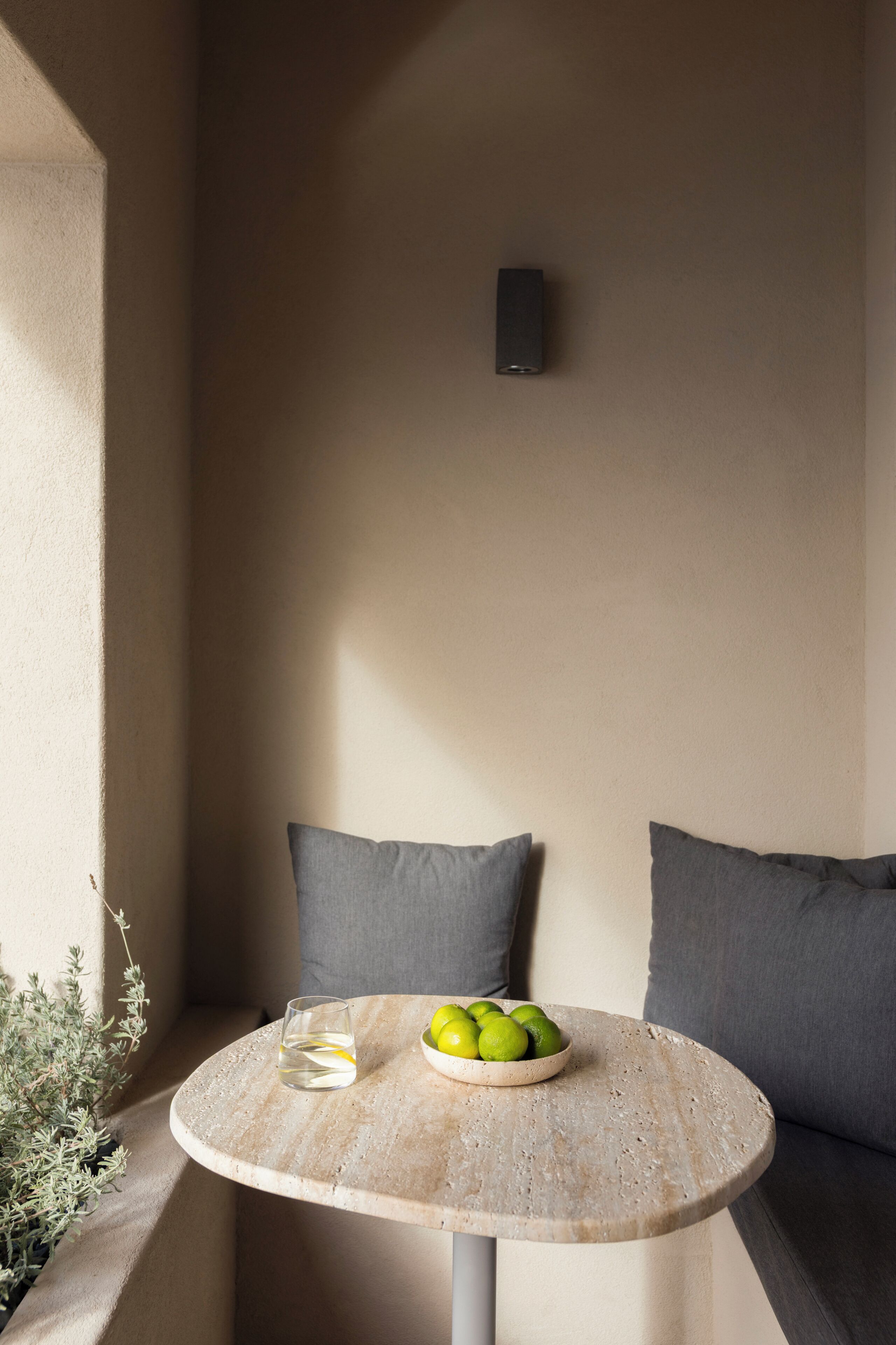 A round table with a bowl of fruit and a glass of water, positioned between two grey cushions.