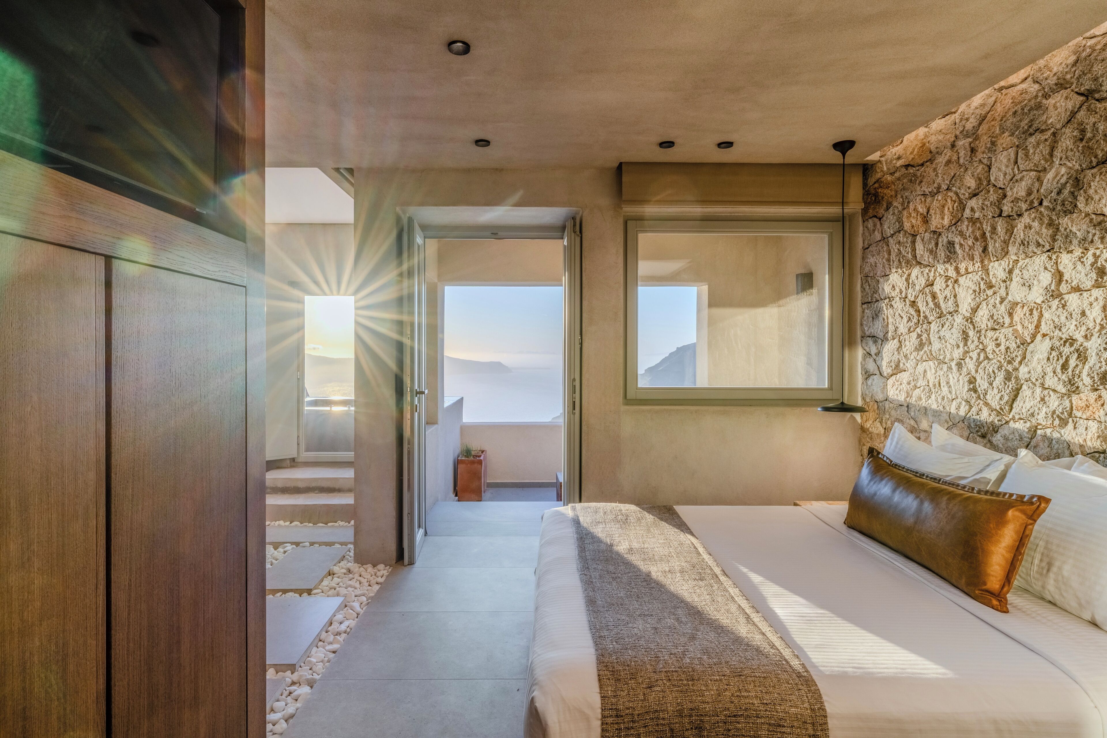 A bedroom with a bed, a stone wall, a window, and a view of the sky.