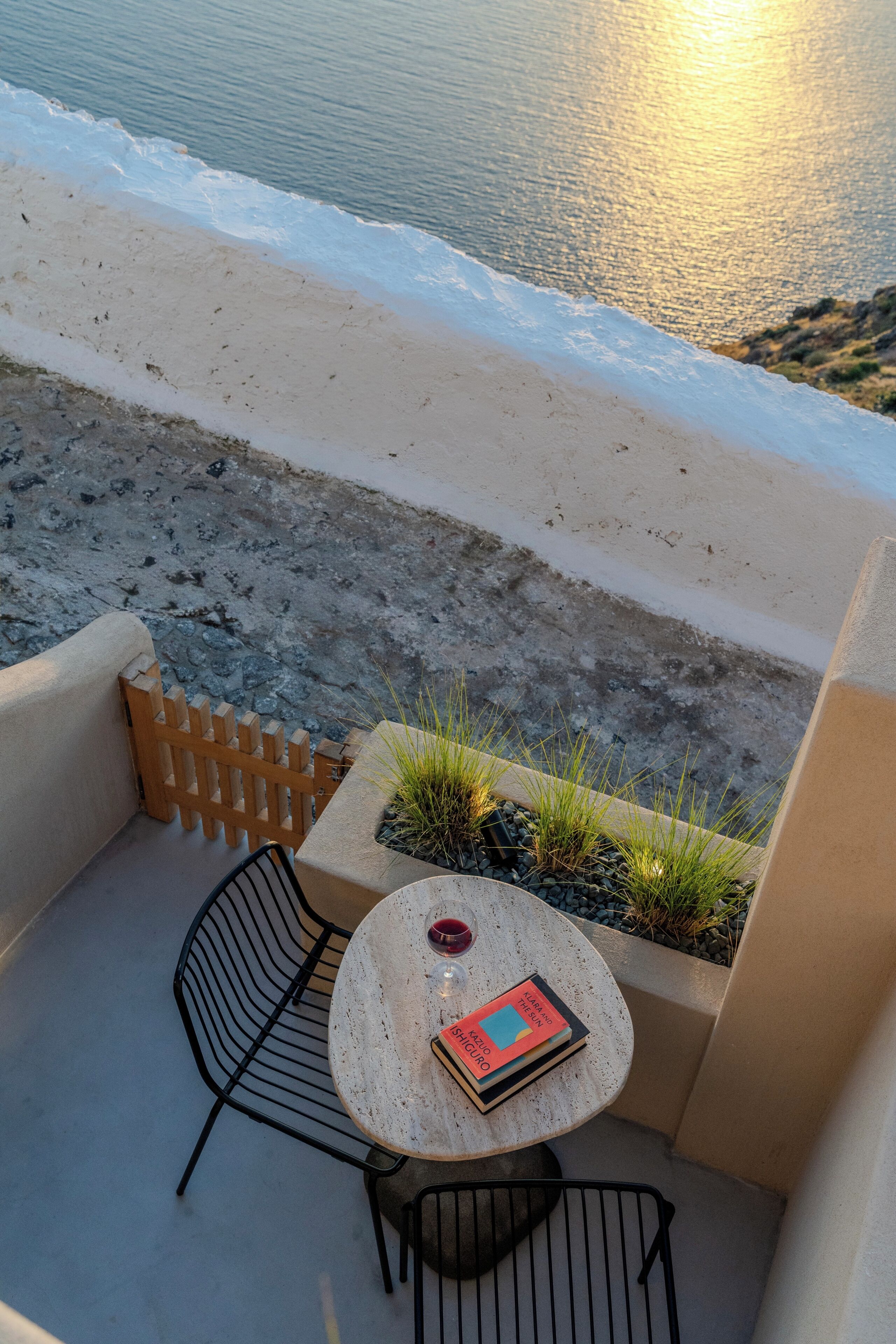 A balcony with a round table, two chairs, a potted plant, and a book.