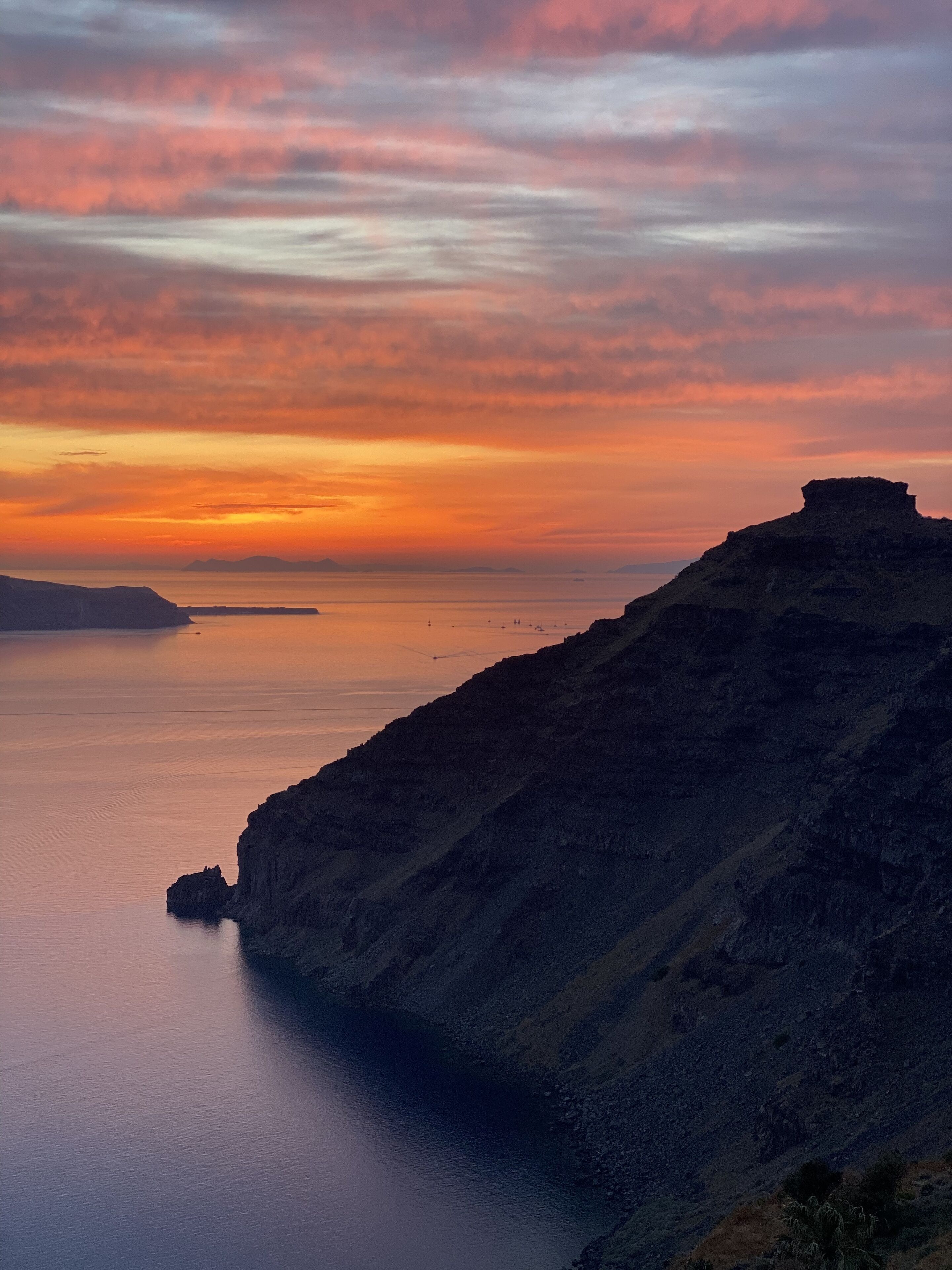 A coastal landscape with a prominent cliff and calm sea during sunset.
