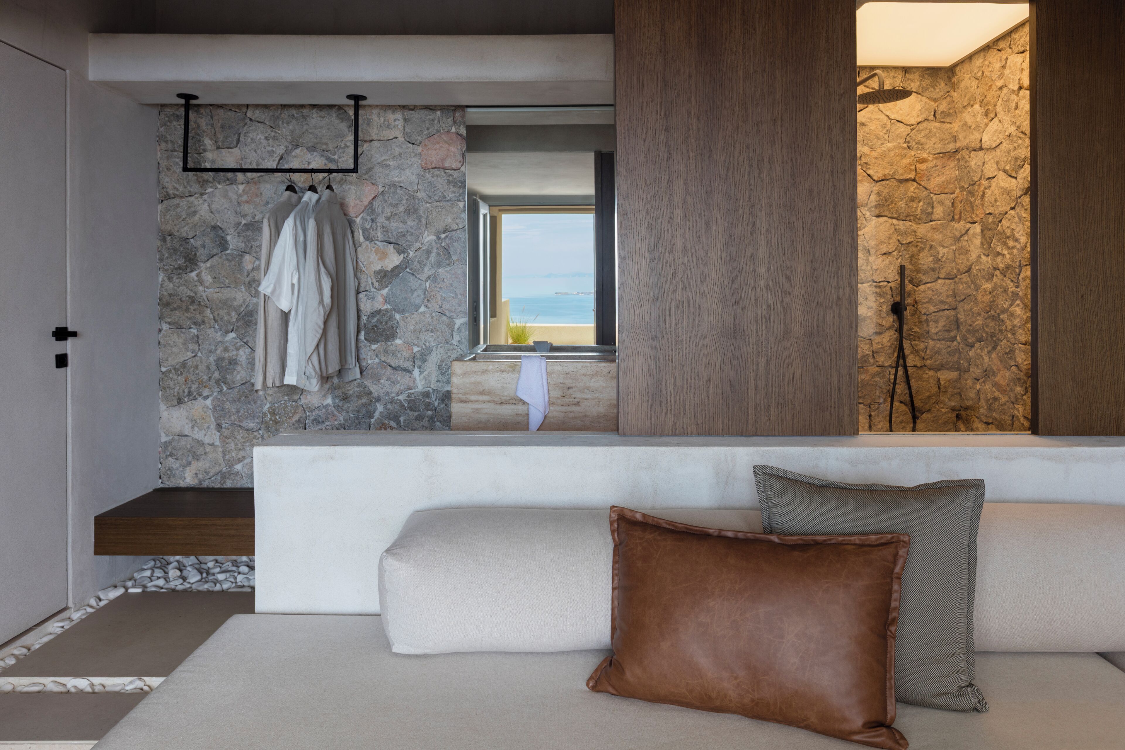 A modern interior with a stone wall, a white sofa, and a view of the sea.