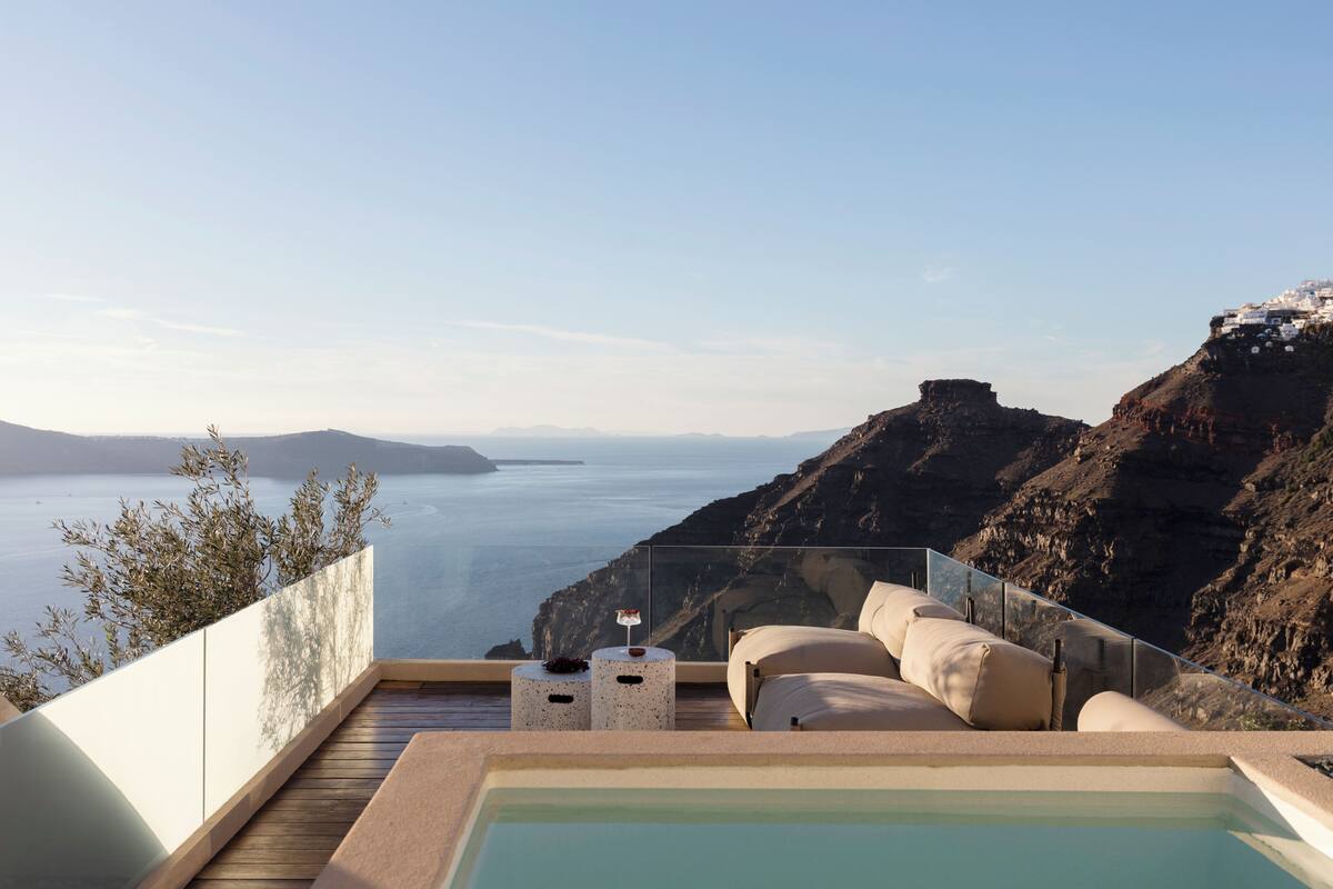 A balcony with a view of the sea, a pool, and a seating area with cushions.