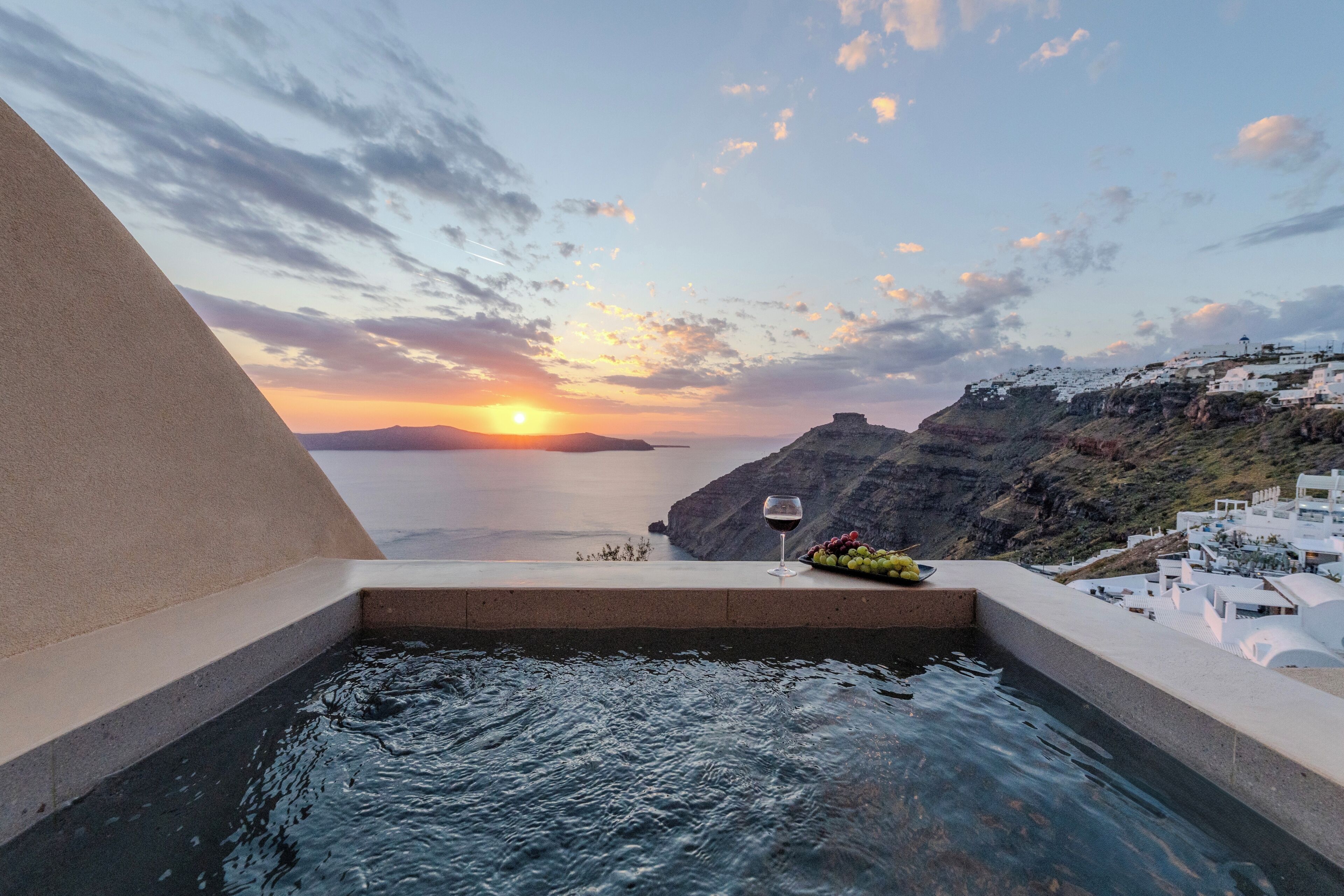 A pool with a sunset view, a glass of wine, and a bowl of fruit.