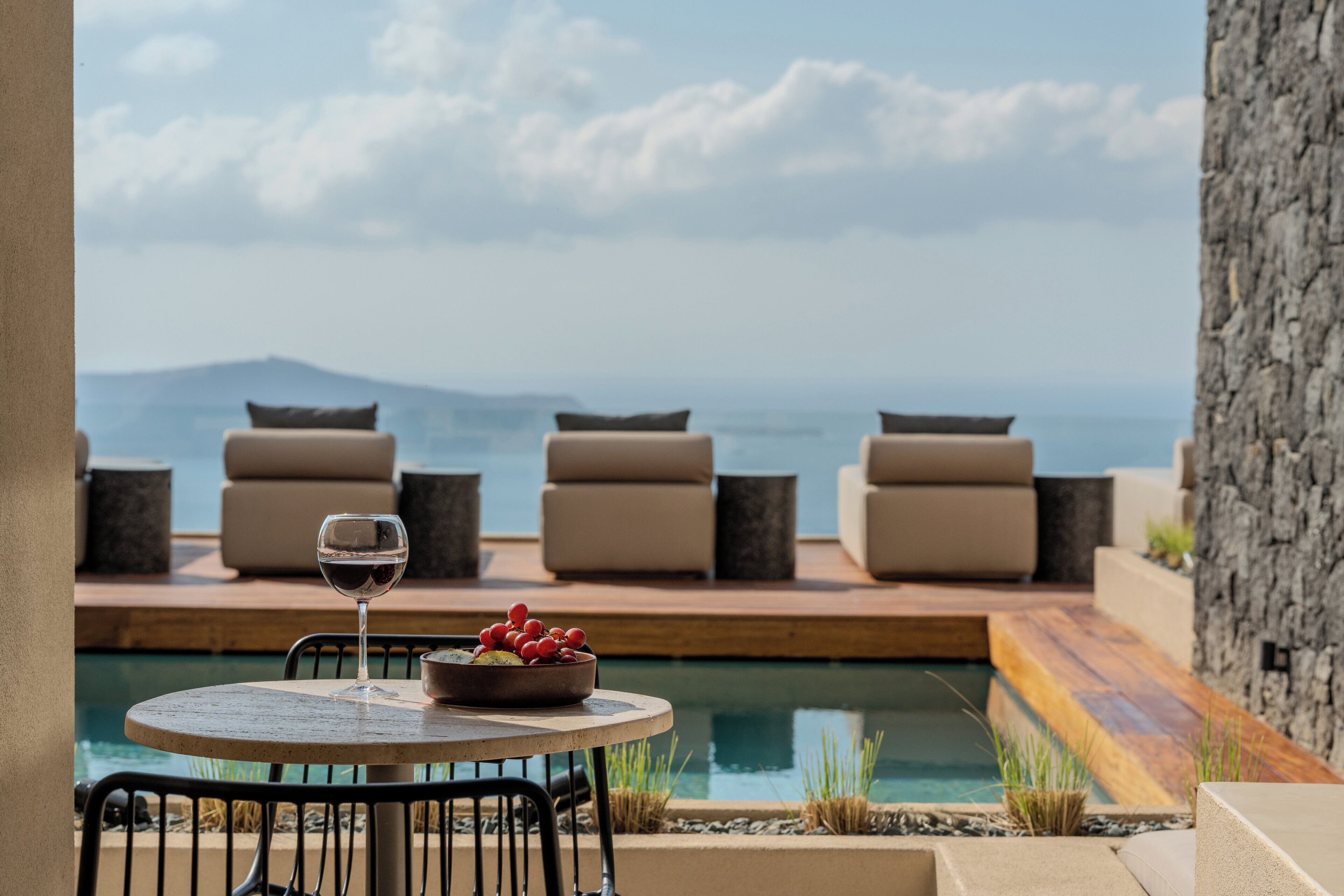 A poolside area with a table, chairs, and a glass of wine.