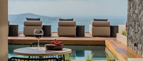 A poolside area with a table, chairs, and a glass of wine.