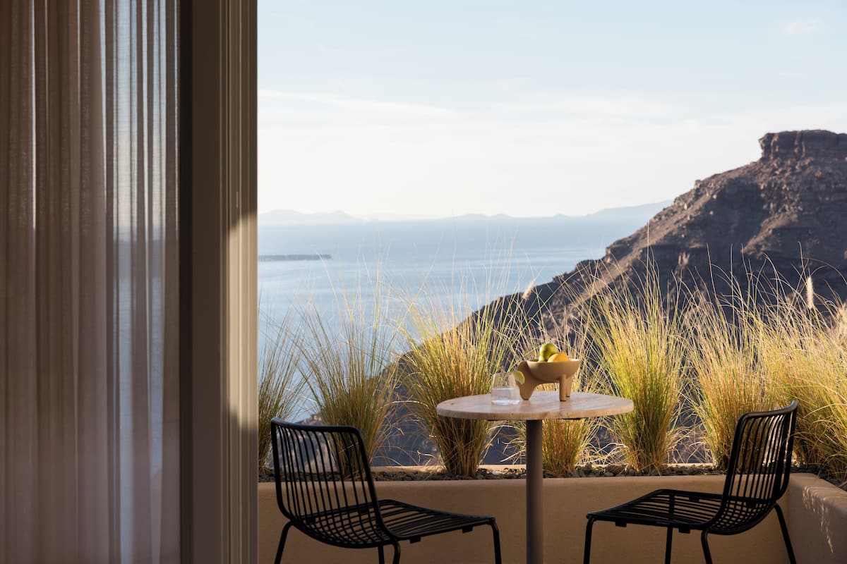A room with a view of a coastal landscape, featuring a round table and two chairs.