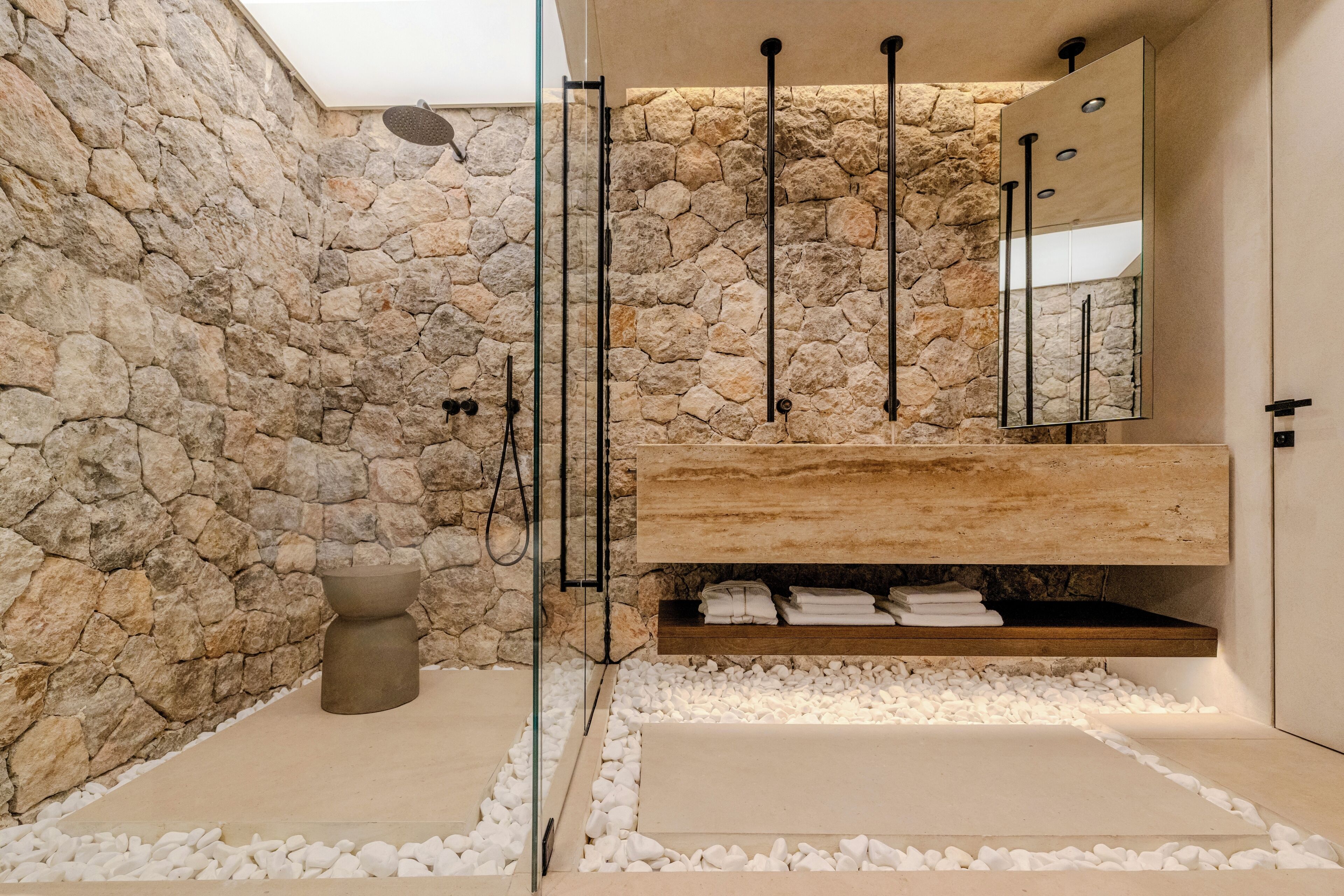 Un baño moderno con paredes de piedra, una bañera independiente y un tocador empotrado.