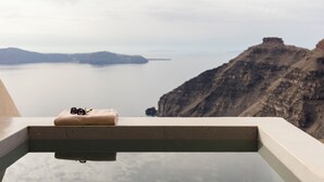 Un balcón con una toalla y gafas de sol, con vista al agua y un acantilado.