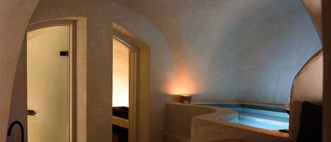 A cozy, dimly lit room with a bathtub, a door leading to another room, and a small table with a lamp.