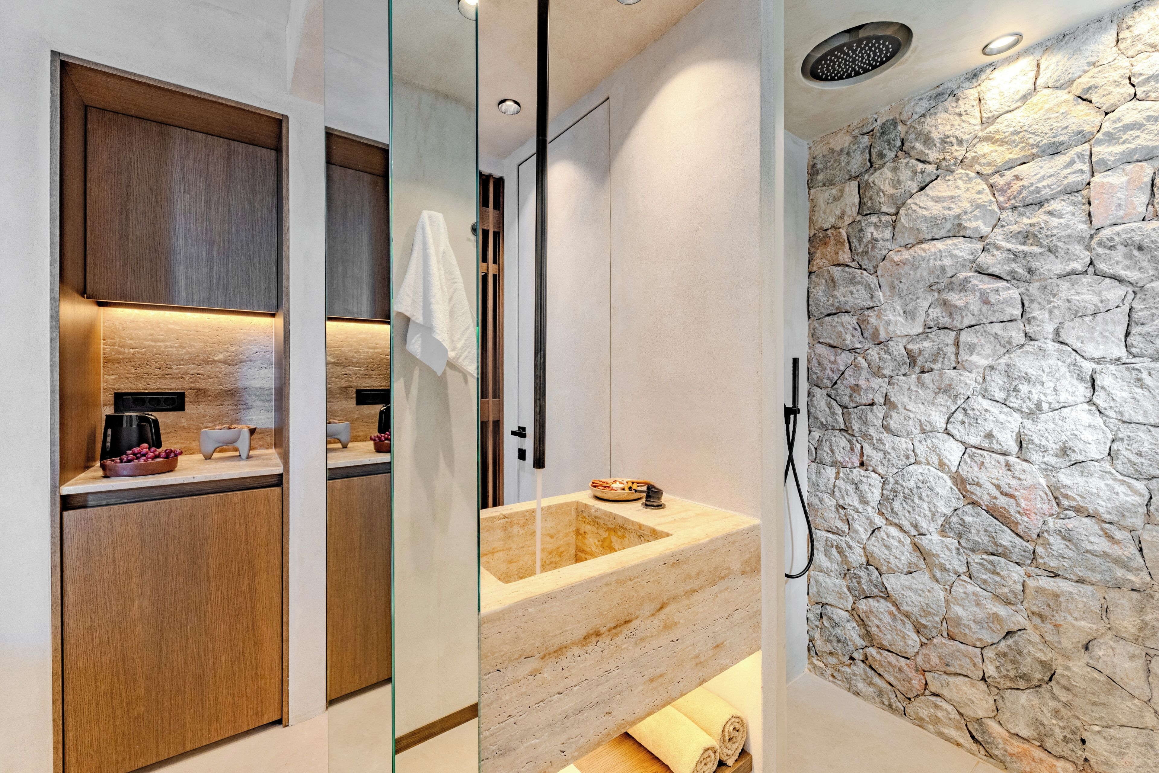 Un baño moderno con pared de piedra, tocador de madera y zona de ducha con mampara de cristal.