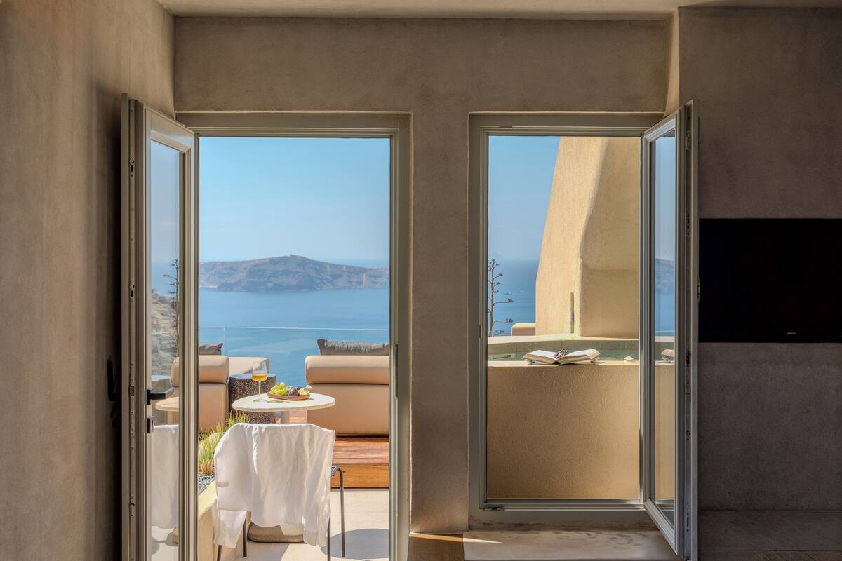 A modern room with a glass door leading to a balcony with a view of the sea and mountains.