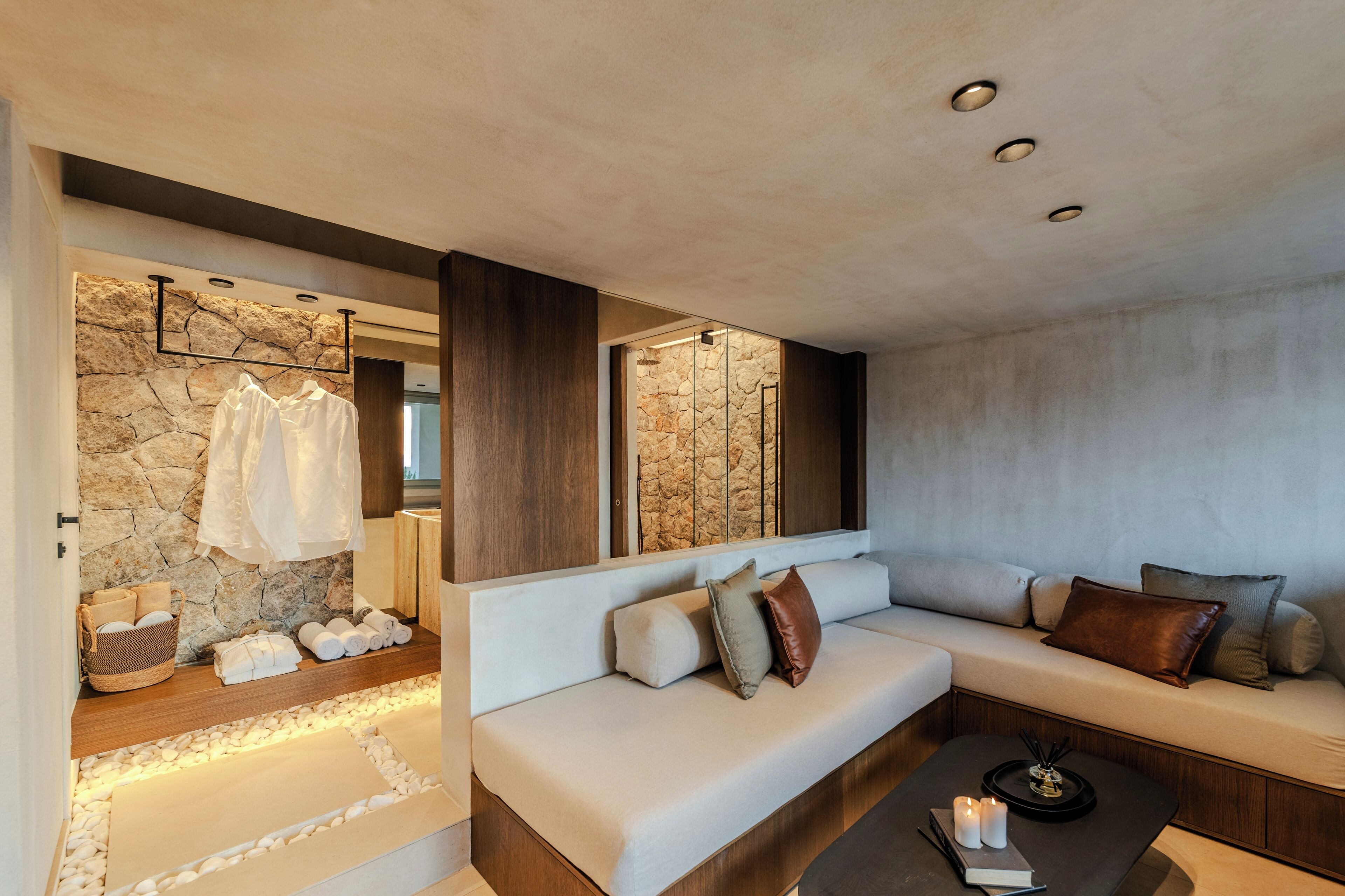A modern living room with a stone wall, a wooden bench, a sofa with cushions, and a coffee table with candles.