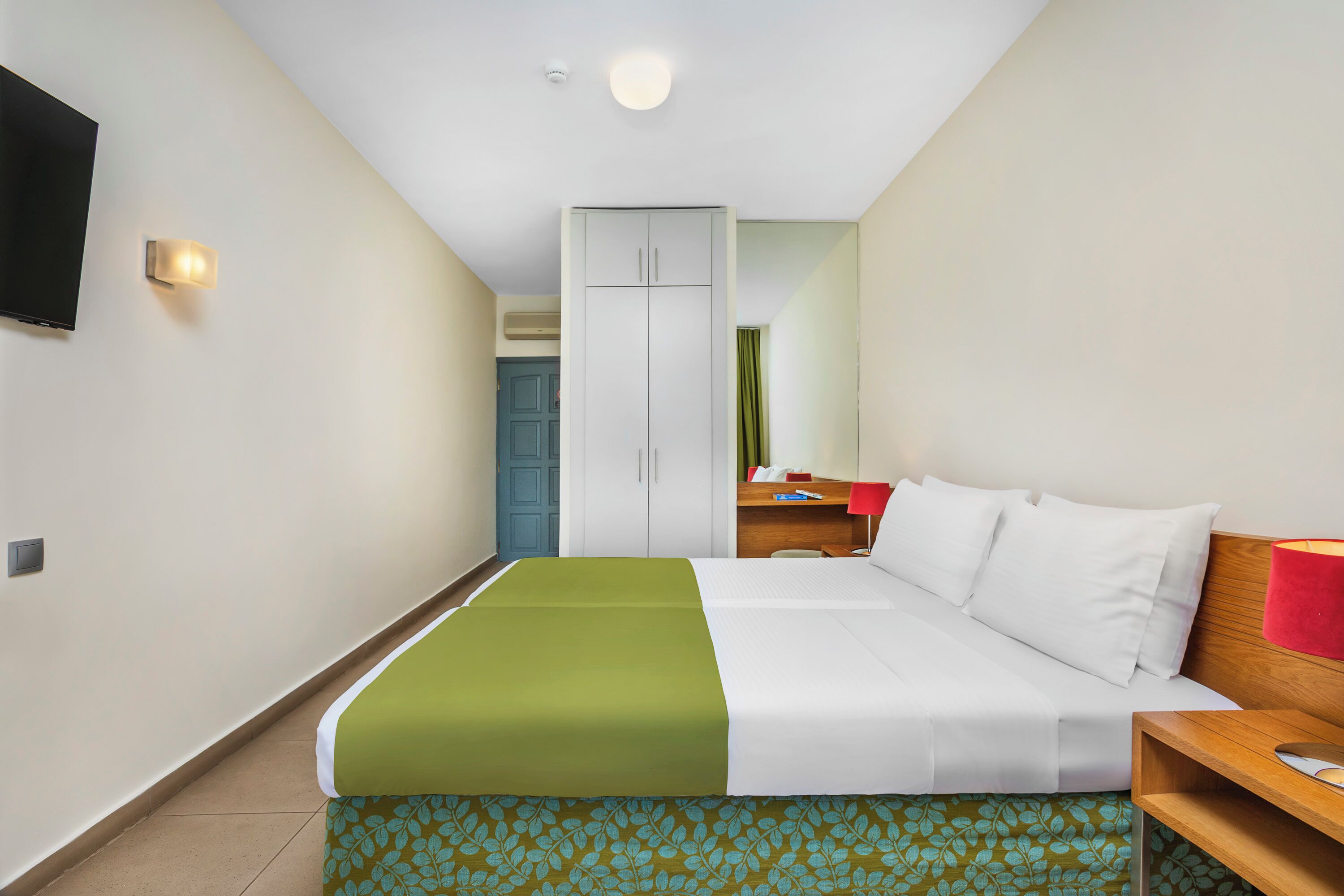 Una habitación de hotel con una cama, un escritorio, un armario y un televisor.