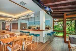 A modern bar area with a wooden ceiling, bar stools, and a view of greenery outside. - Hanioti Village Resort (Kassandra)