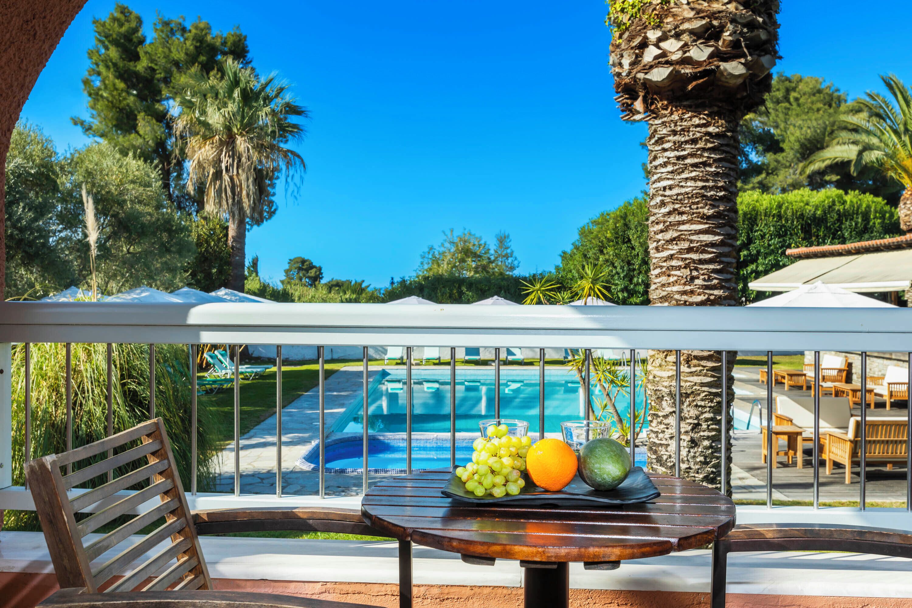 A balcony with a table holding fruit, overlooking a swimming pool and outdoor seating area.