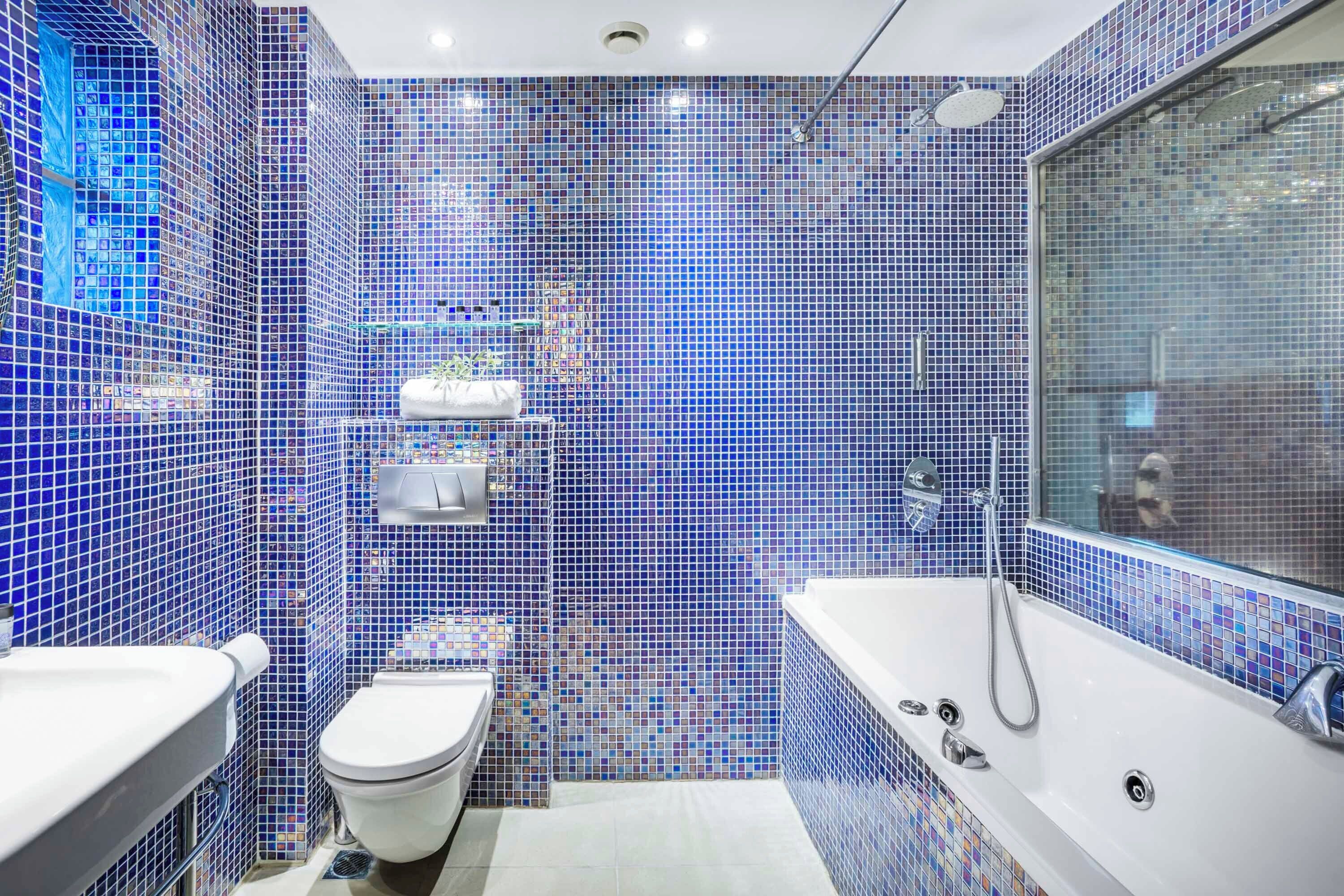 A bathroom with a mosaic tile wall, a bathtub, a toilet, and a sink.