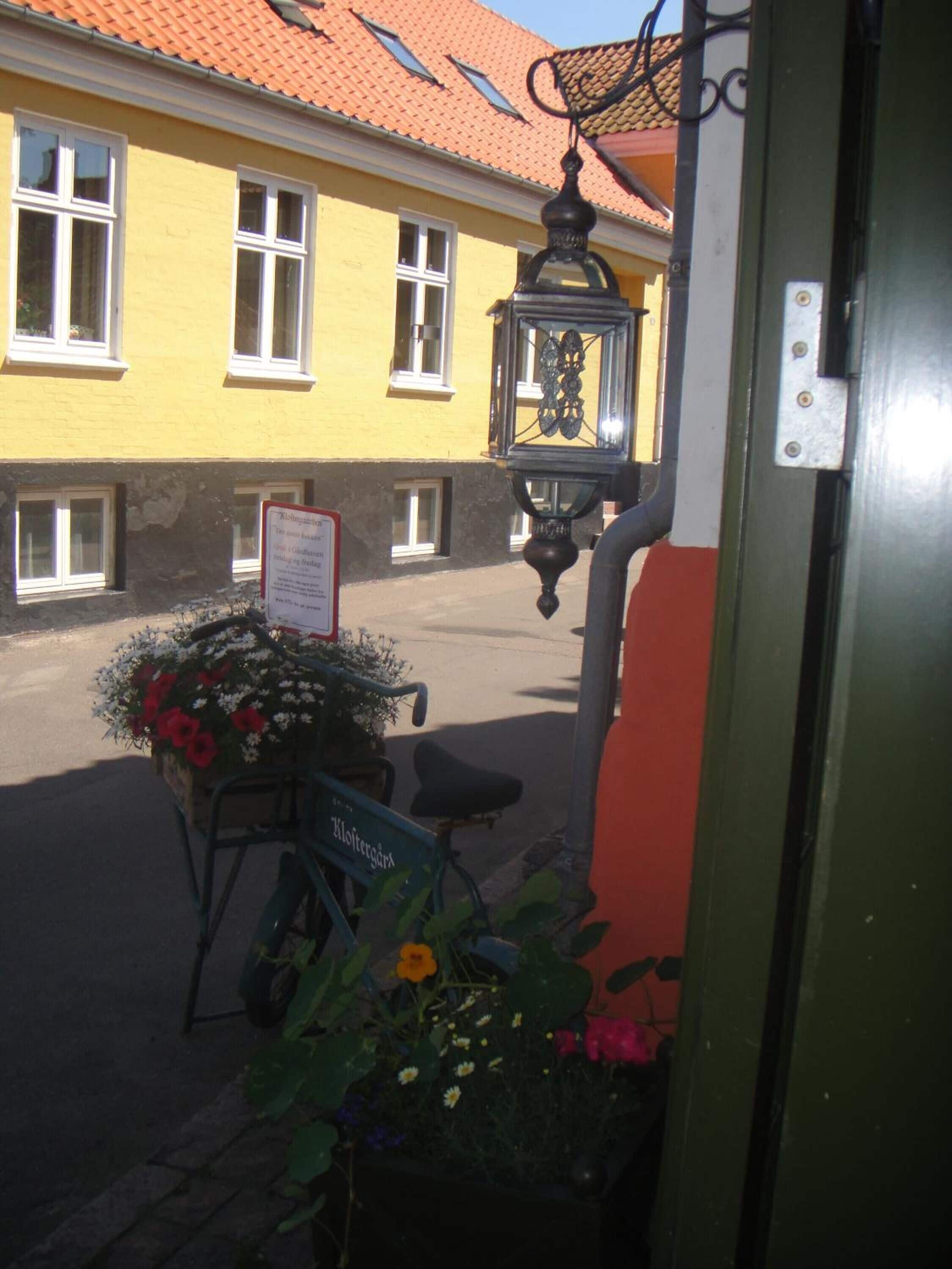 A yellow building with a red-tiled roof, a signboard, and a bicycle with a basket of flowers.