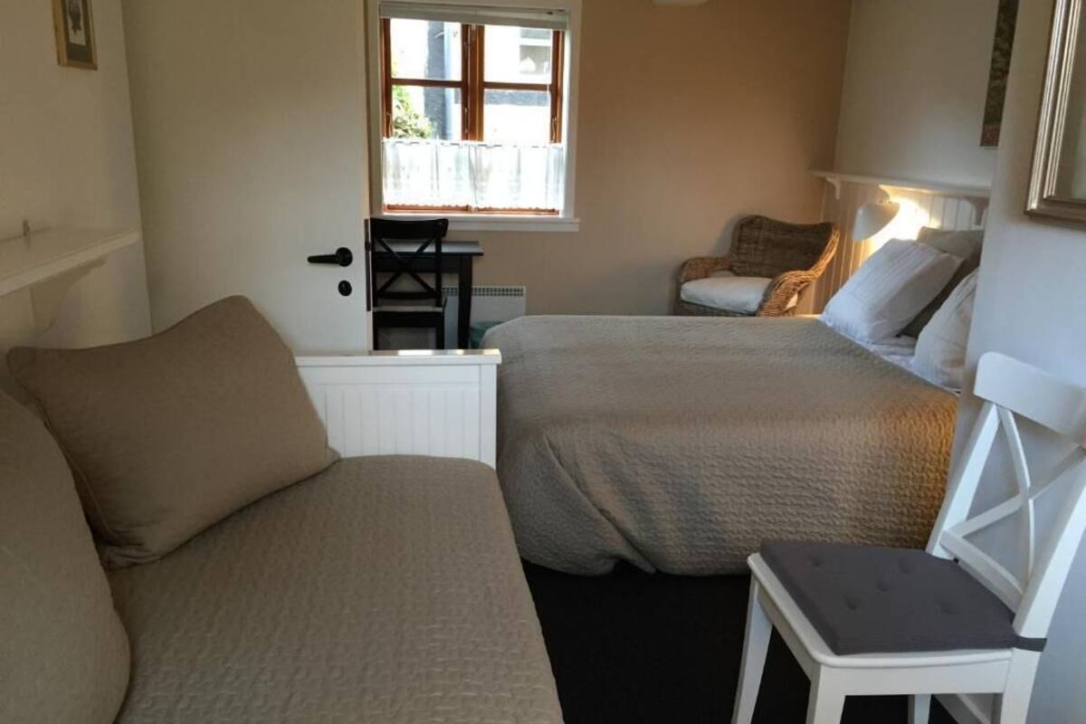 A bedroom with two beds, a chair, a window, and a radiator.