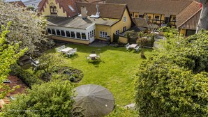 A courtyard with a lawn, outdoor seating, and a building with a traditional design. - Hotel Klostergaarden (Allinge)