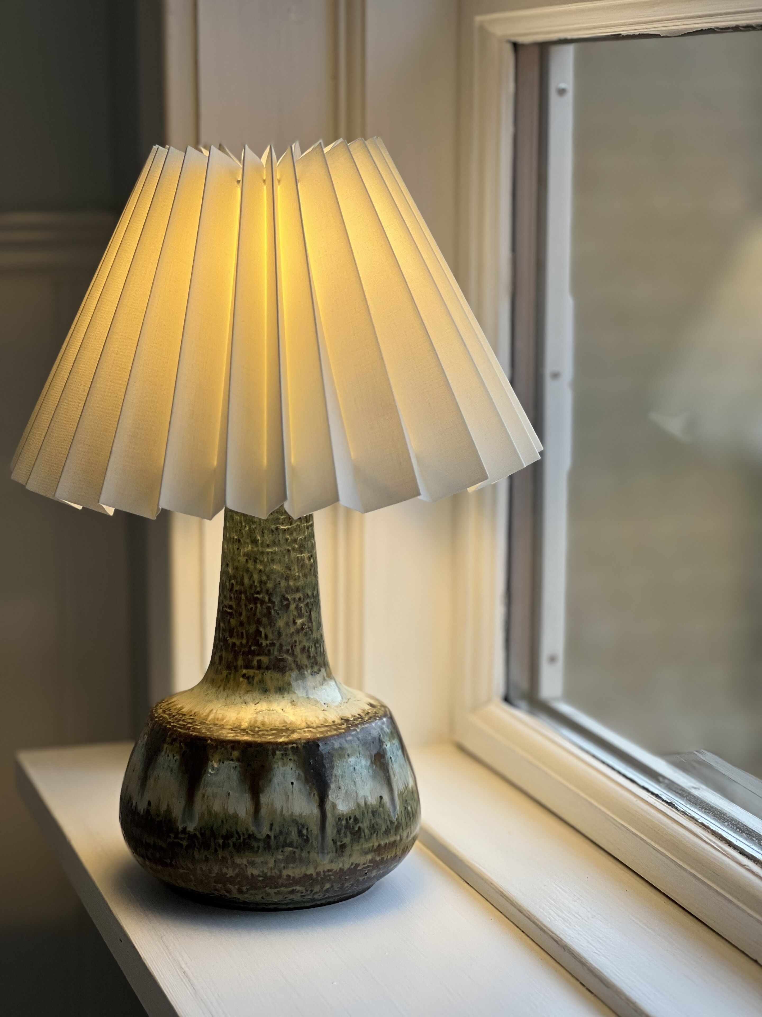 A table lamp with a pleated shade on a windowsill.