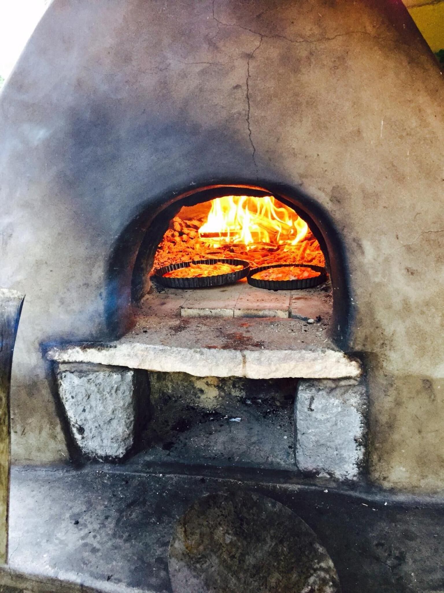 Tiilestä rakennettu uuni, jonka sisällä on kaksi pizzapeltiä, ja jossa näkyy liekit. Uunin pohja on betonista.