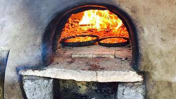 Tiilestä rakennettu uuni, jonka sisällä on kaksi pizzapeltiä, ja jossa näkyy liekit. Uunin pohja on betonista.