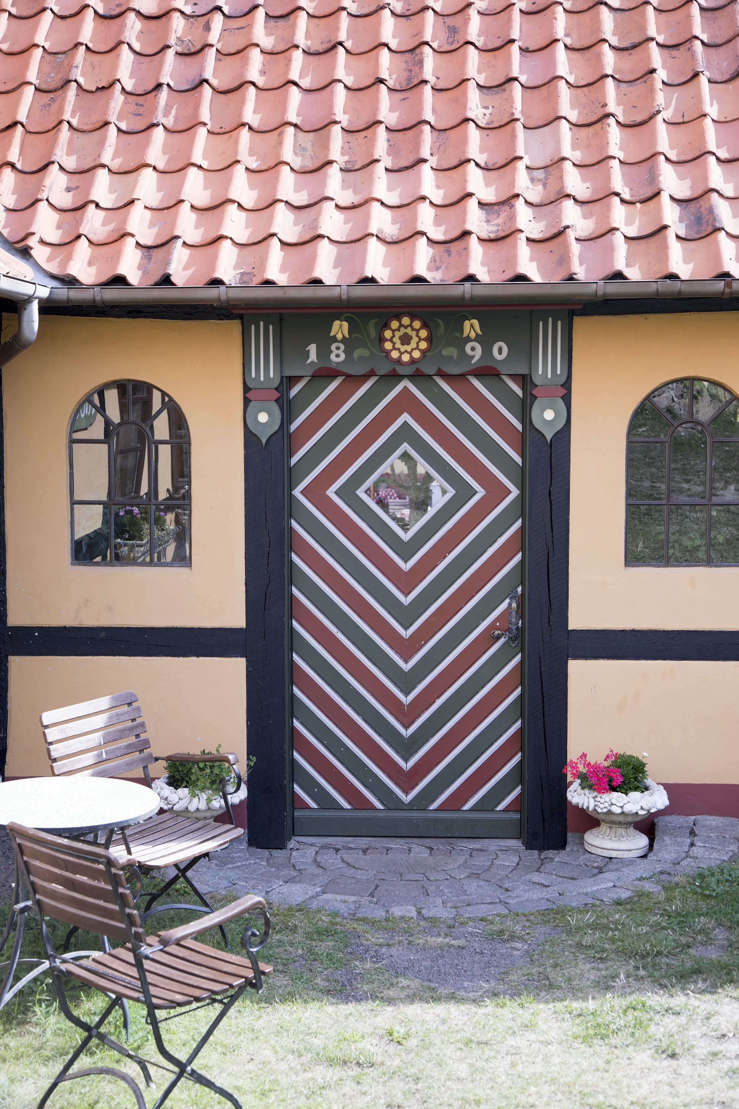 A building with a tiled roof, a decorative door with geometric patterns, and a small outdoor seating area with a table and chairs.