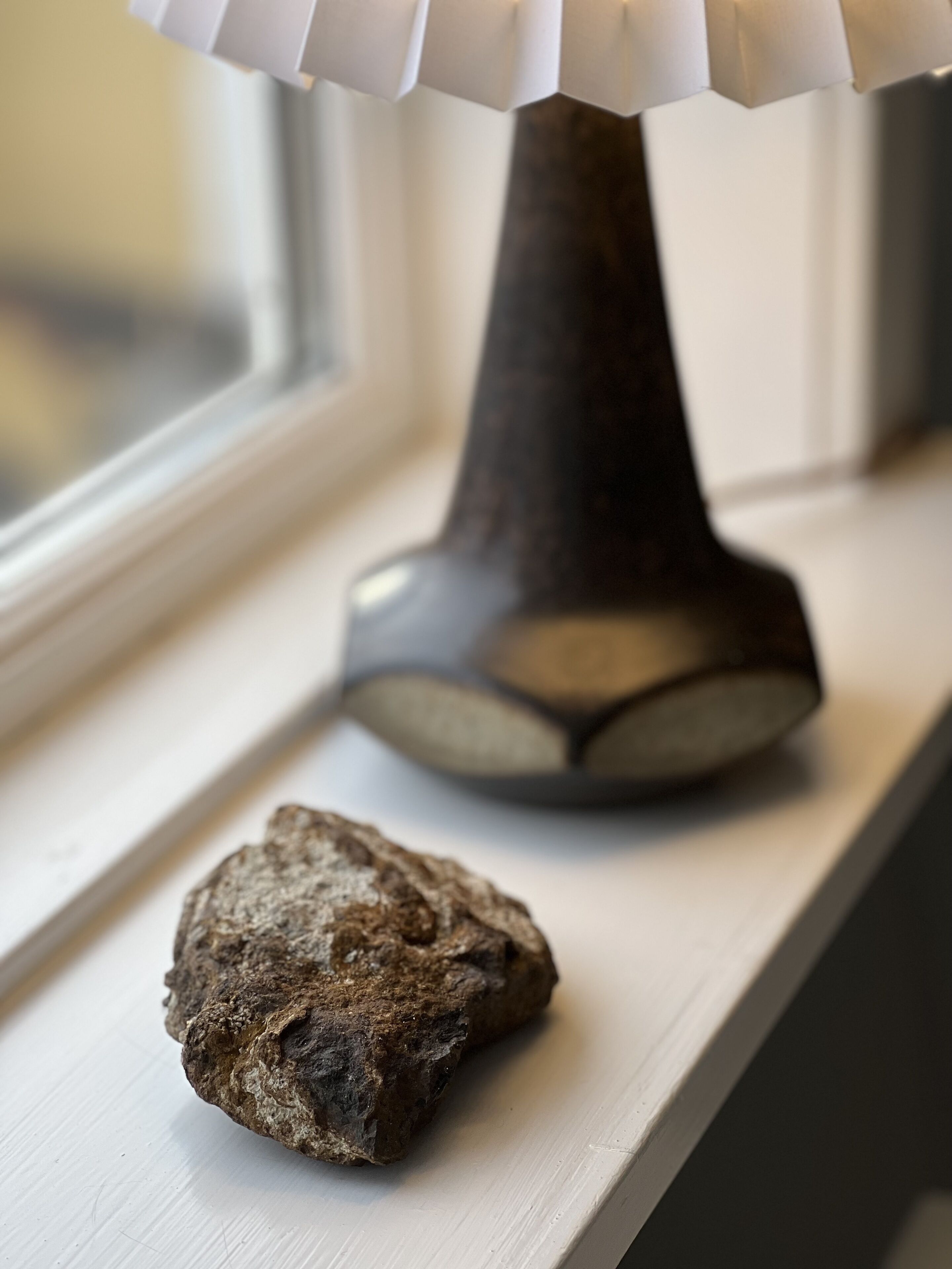 A lamp and a rock on a window sill.