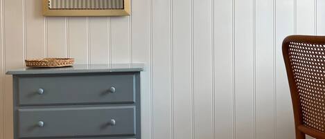 Una habitación con tocador, espejo, perchero de madera y una silla.